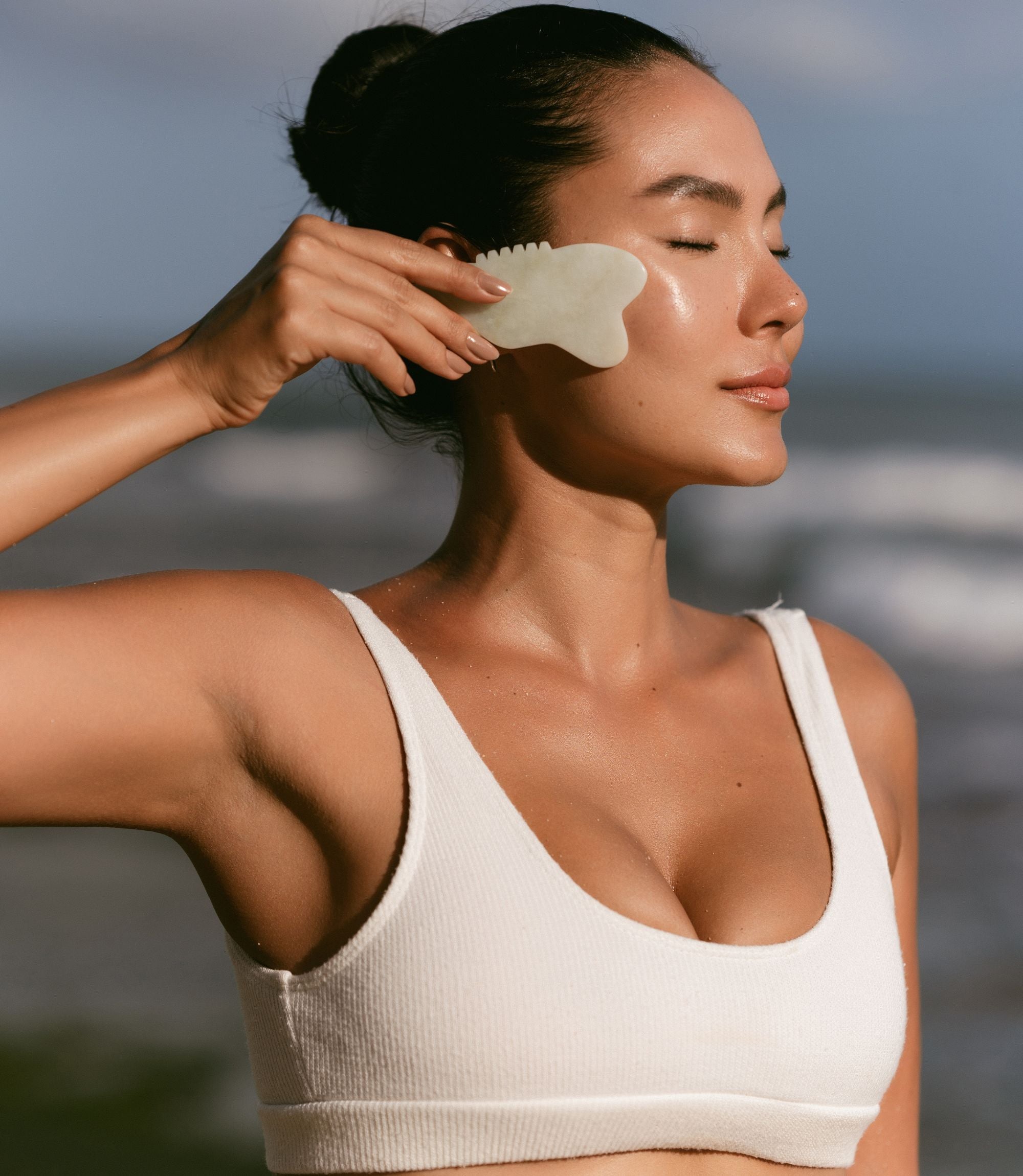 girl_holding_a_gua_sha_tool_across_her_face_in_white_bathing_suit.jpg