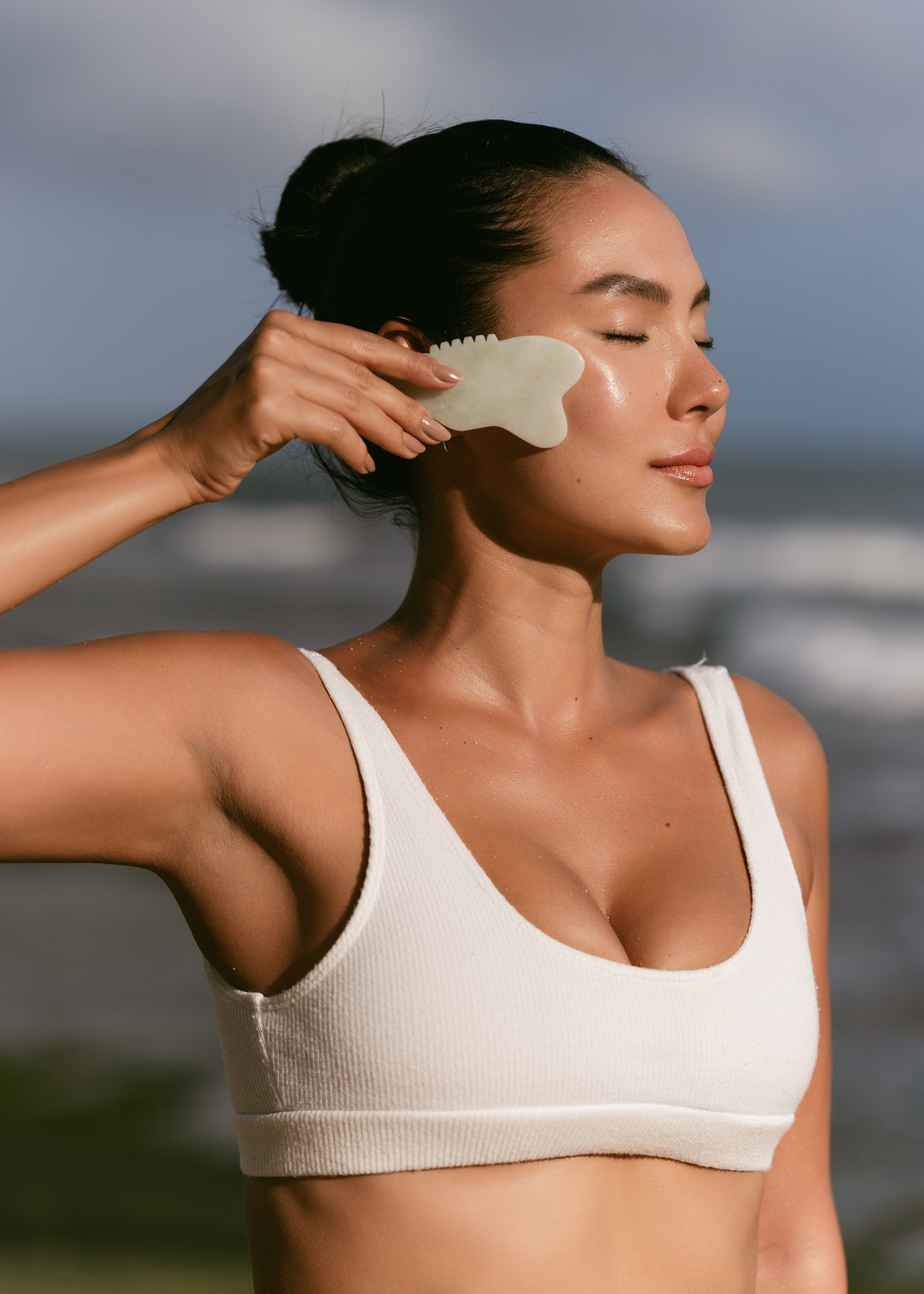 girl_holding_a_gua_sha_tool_across_her_face_in_white_bathing_suit.jpg