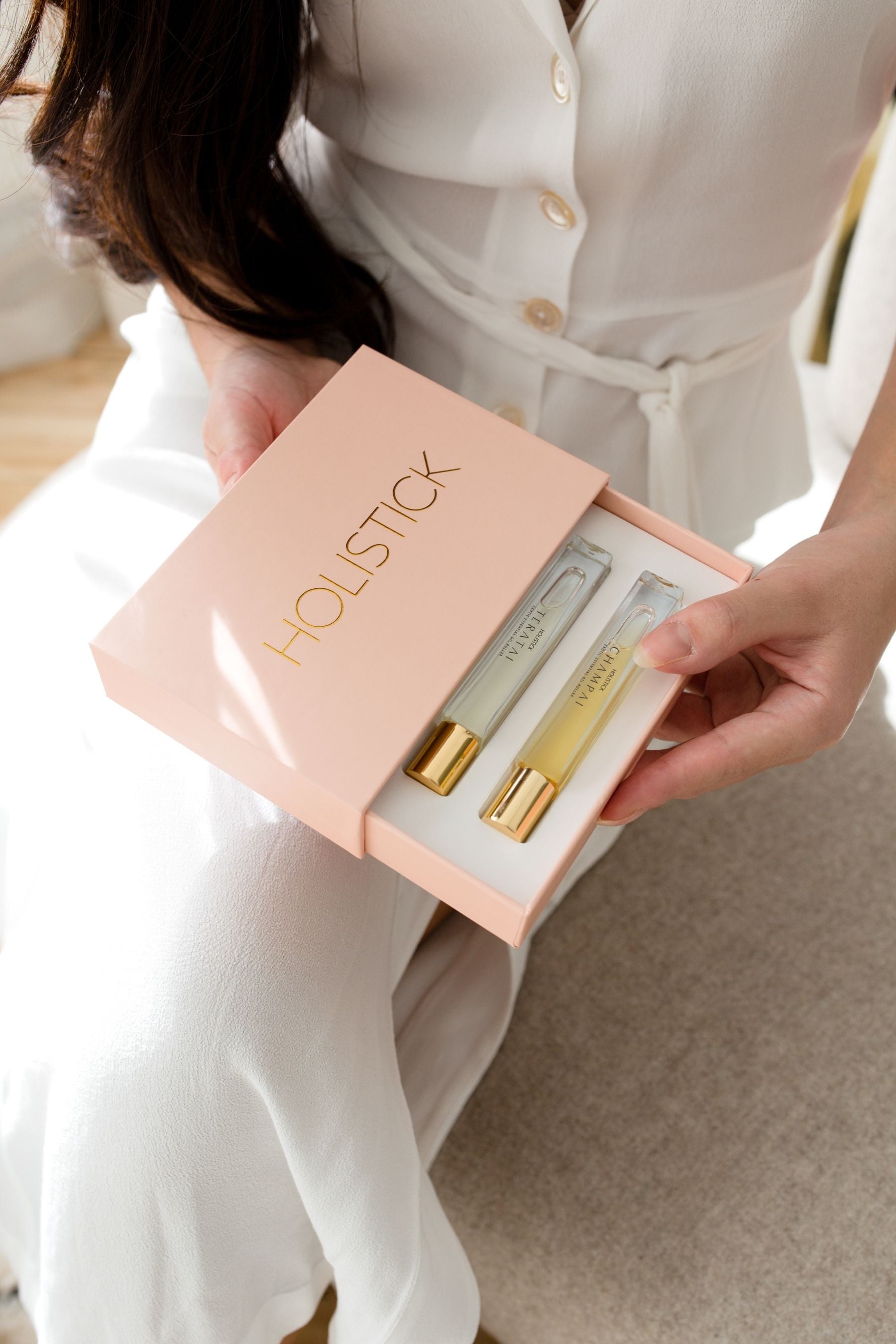 Girl in white dress holding Holistick 3 piece natural essential oil perfume set in packaging